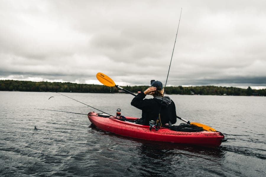 A fishing rod resting across the deck of a kayak on calm water